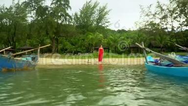冒险背景。 岛上海岸的传统蓝色渔船.. 穿着红色裙子的女人走在